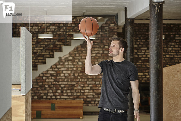 Junger Mann im Büro spielt mit Basketball