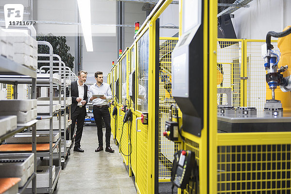 Zwei Geschäftsleute beobachten Industrieroboter in der Fabrik