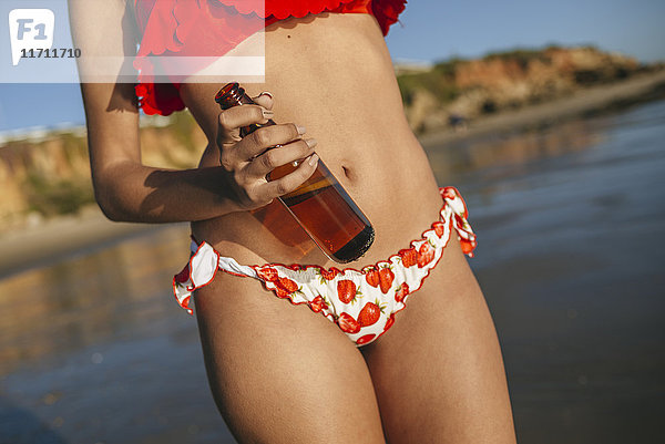Junge Frau mit Bierflasche am Strand  Teilansicht