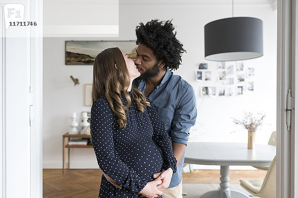 Küssen eines schwangeren Paares im Wohnzimmer
