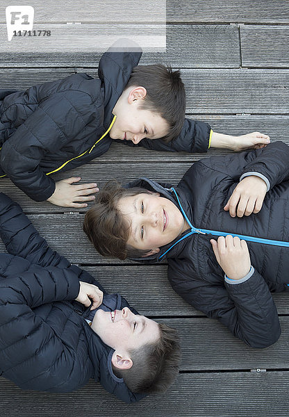 Drei Freunde in schwarzen Kapuzenjacken auf der Terrasse liegend