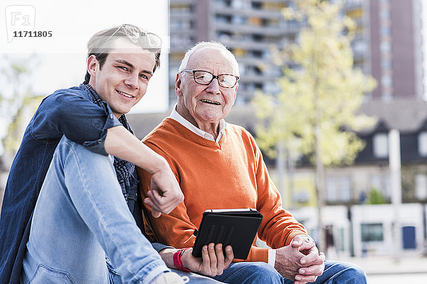 Porträt eines lächelnden älteren Mannes und erwachsenen Enkels mit Tablette