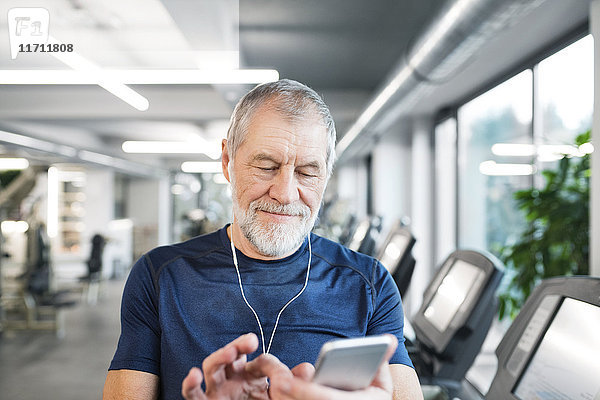 Senior Mann mit Smartphone und Kopfhörer im Fitnessstudio