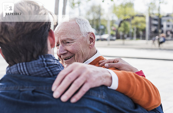 Lächelnder älterer Mann  der den erwachsenen Enkel im Freien ansieht.