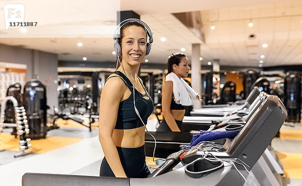 Lächelnde Frau mit Kopfhörer im Fitnessstudio auf einem Treadmil