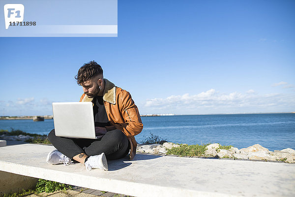 Spanien  Cadiz  Junger Mann am Hafen mit Laptop