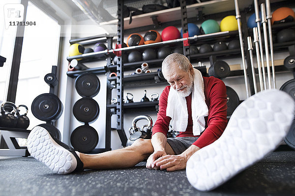 Erschöpfter älterer Mann  der nach dem Training im Fitnessstudio auf dem Boden sitzt.