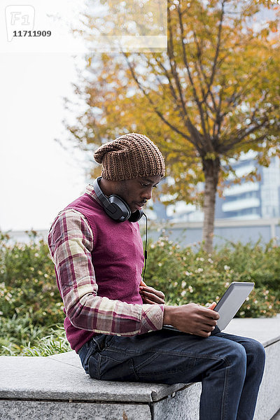 Mann mit Kopfhörer auf der Bank sitzend  mit Blick auf den Laptop