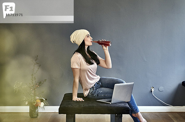 Junge Frau mit Laptop beim Trinken aus der Flasche