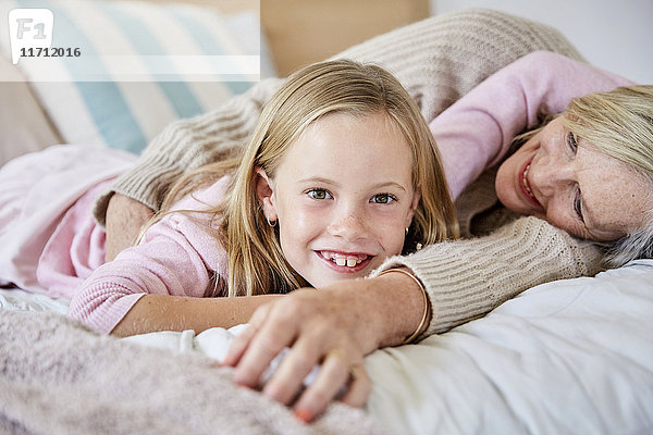 Porträt eines glücklichen kleinen Mädchens  das mit seiner Großmutter auf dem Bett liegt.