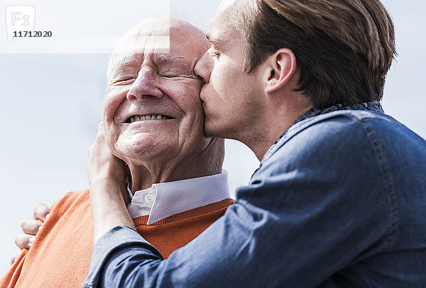 Erwachsener Enkel  der den älteren Mann im Freien küsst.
