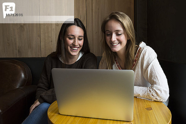 Zwei lächelnde Freunde  die in einem Café sitzen und auf den Laptop schauen.
