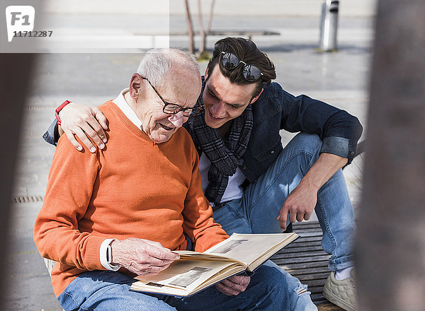 Senior Mann und erwachsener Enkel auf einer Bank beim Betrachten des Fotoalbums