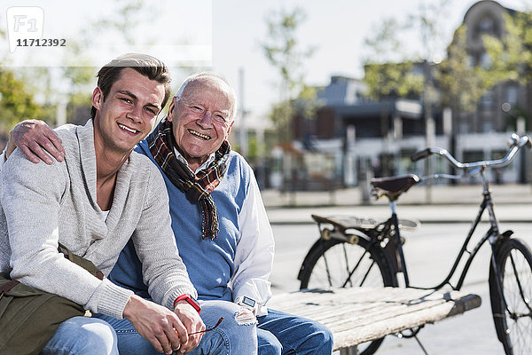 Portrait eines glücklichen älteren Mannes mit erwachsenem Enkel auf einer Bank sitzend