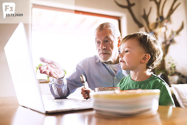 Großvater und Enkel sitzen am Tisch  essen und benutzen Laptop