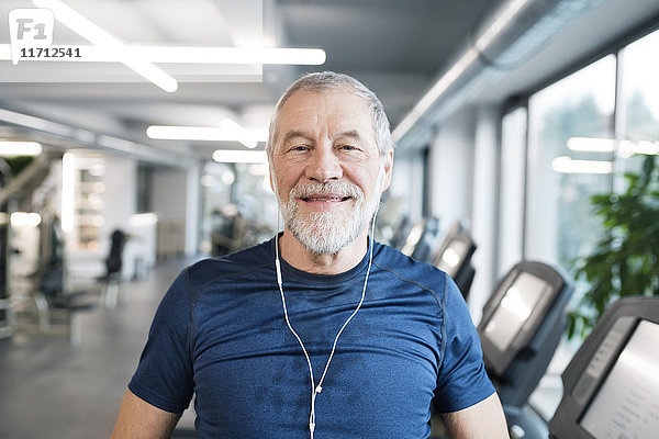 Portrait eines fitten Senioren mit Kopfhörern im Fitnessstudio