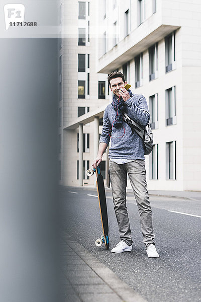 Geschäftsmann mit Skateboard  mit Smartphone und Kopfhörer