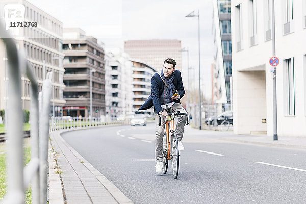 Geschäftsmann auf dem Fahrrad in der Stadt  mit Smartphone und Kopfhörer