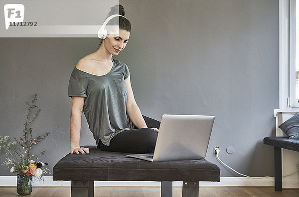 Junge Frau mit Kopfhörer im Wohnzimmer mit Laptop