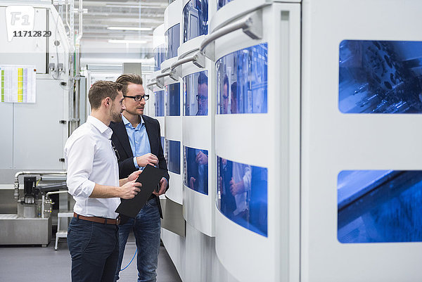 Zwei Männer  die in der Fabrikhalle reden und die Maschine ansehen.