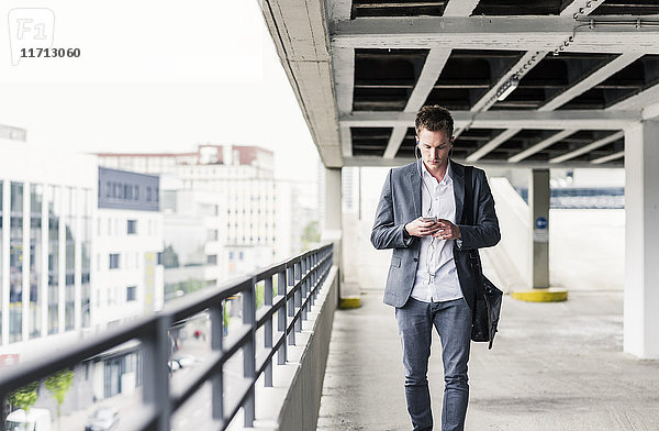 Junger Geschäftsmann mit Smartphone  zu Fuß auf Parkebene