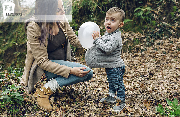 Glückliche schwangere Mutter und kleiner Junge  die Spaß mit einem Ballon im Wald haben.