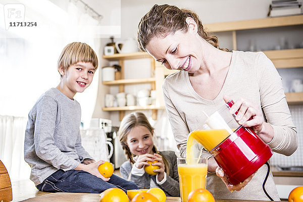 Frau gießt frisch gepressten Orangensaft ins Glas für Kinder