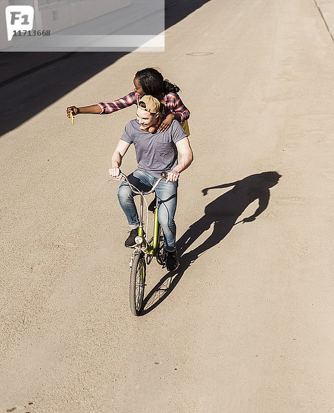 Junger Mann auf dem Fahrrad mit seiner Freundin  die auf einem Gestell steht und sich selbst nimmt
