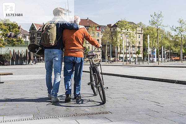 Senior mit Fahrrad und erwachsenem Enkel in der Stadt unterwegs
