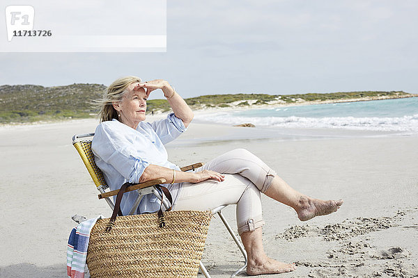 Seniorin sitzt am Strand und schaut in die Ferne.
