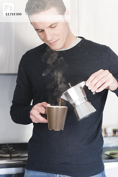 Mann gießt heißen Espresso in eine Tasse in der Küche