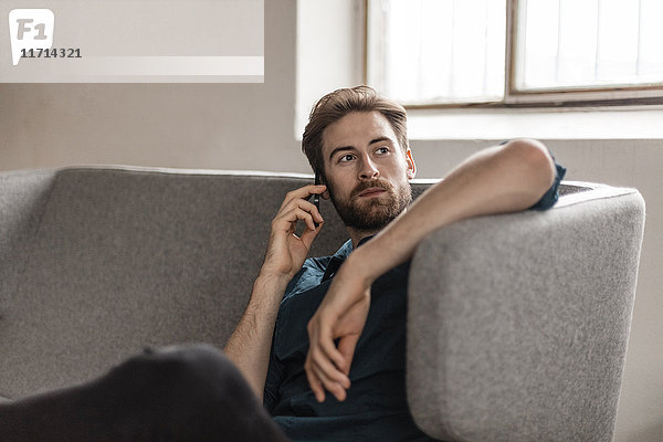Porträt eines jungen Mannes am Telefon  der auf der Couch sitzt.