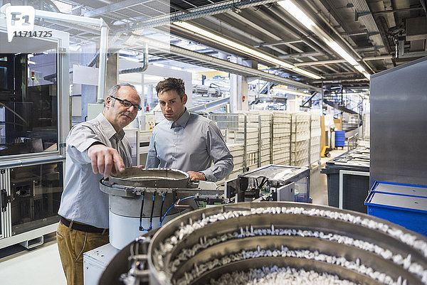 Zwei Männer in der Fabrikhalle untersuchen das Ergebnis einer Maschine