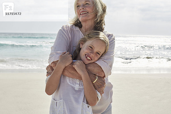Großmutter umarmt Enkelin am Strand