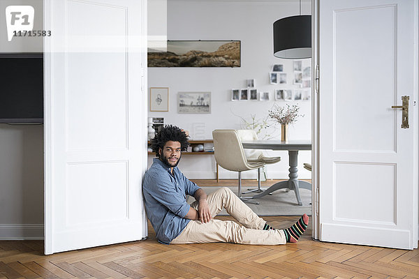 Mann zu Hause auf dem Boden sitzend auf Türrahmen im Wohnzimmer lehnend