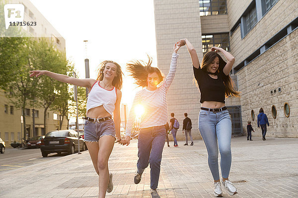Drei glückliche junge Frauen laufen Hand in Hand auf dem Bürgersteig.