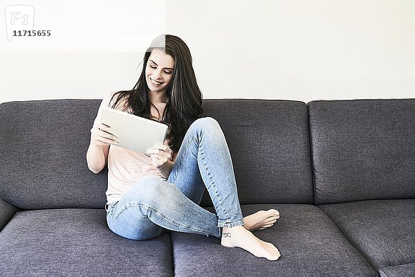 Lächelnde junge Frau auf der Couch sitzend mit Tablette