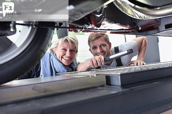 Porträt eines lächelnden Automechanikers mit Kunde in der Werkstatt am Auto