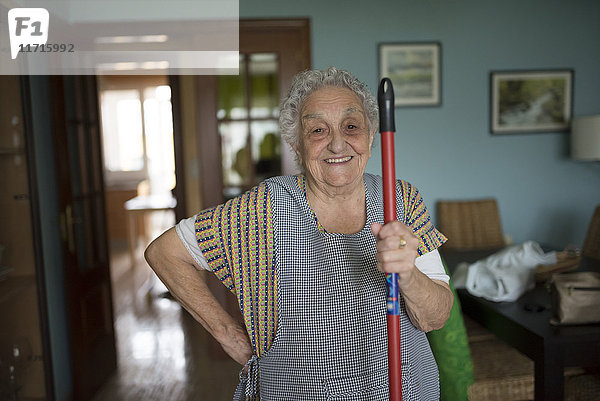 Porträt einer lächelnden Seniorin  die den Wischmopp in der Hand hält.