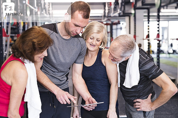 Gruppe von fit Senioren und Personal Trainer im Fitnessstudio mit Blick auf Tablette