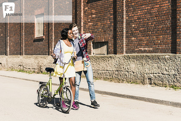 Junges Paar mit Fahrrad und Skateboard  das sich mit dem Smartphone auskennt