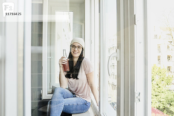 Porträt einer lächelnden jungen Frau mit Flasche am Fenster