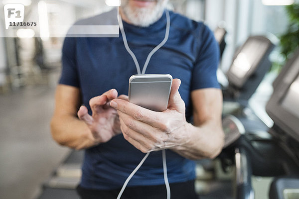 Senior Mann mit Smartphone im Fitnessstudio