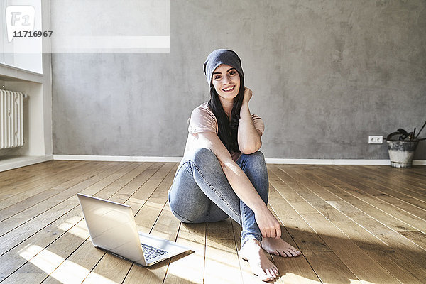 Lächelnde junge Frau auf dem Boden sitzend mit Laptop