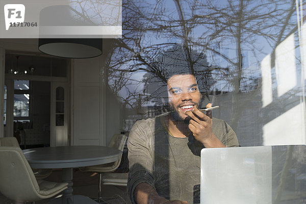 Mann spricht auf dem Smartphone vor dem Laptop am Fenster