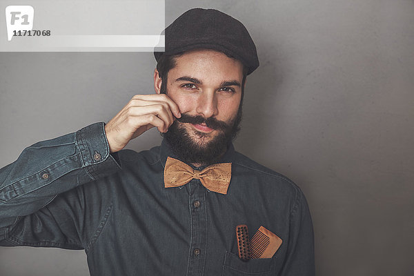 Porträt eines bärtigen Mannes mit Mütze  Jeanshemd  Kork-Fliege  Holzkamm für Bart und Schnurrbart in der Tasche.