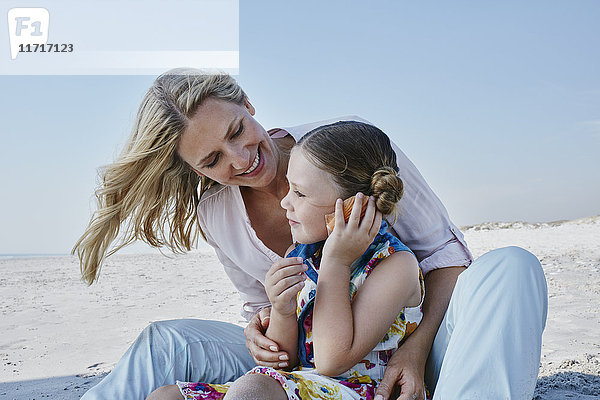 Glückliche Mutter und Tochter mit Muschel am Strand