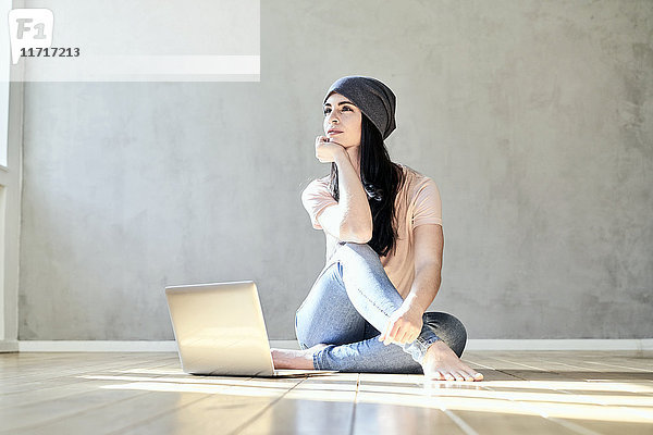 Nachdenkliche junge Frau auf dem Boden sitzend mit Laptop