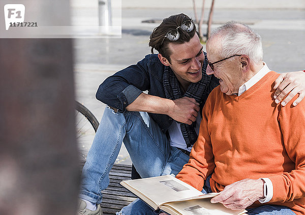 Glücklicher älterer Mann und erwachsener Enkel mit Fotoalbum im Freien