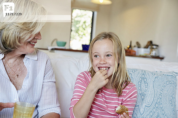 Porträt eines lächelnden kleinen Mädchens  das Sandwich isst  während Großmutter ihr zusieht
